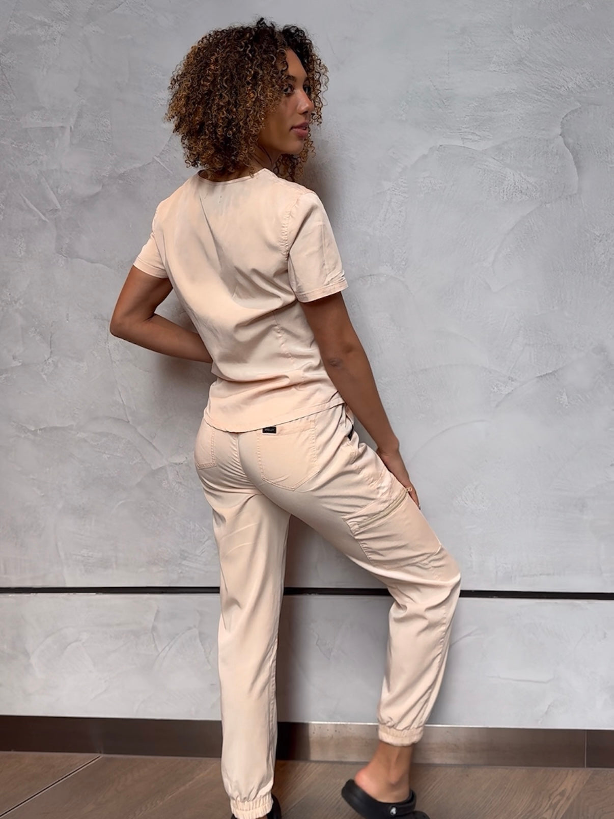 Nurse wearing beige fashionable scrubs. Posing to show the back of the scrubs.